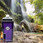 A person standing in front of a waterfall with bottles.