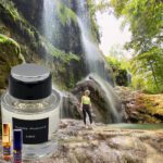 A person standing in front of a waterfall with a bottle.