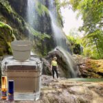 A person standing in front of a waterfall next to a bottle.