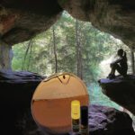 A person sitting on the ground in front of a cave.