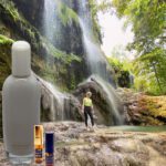 A person standing in front of a waterfall with a bottle.