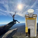 A person jumping in the air over a rock with an empty bottle of perfume.