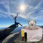 A person jumping in the air over rocks with an open bottle of perfume.