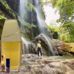 A person standing in front of a waterfall with an oil bottle.