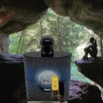 A bottle of perfume and a small container in front of a cave.