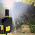 A bottle of perfume and a vial in front of a waterfall.