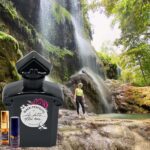 A man standing in front of a waterfall next to a bottle.