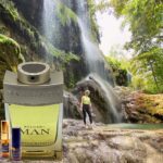 A man standing next to a waterfall with a bottle of perfume.