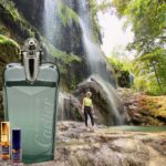 A man standing in front of a waterfall next to a bottle.