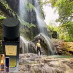 A person standing in front of a waterfall with bottles.