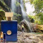 A man standing next to a waterfall near a bottle of perfume.