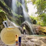 A person standing in front of a waterfall with a bottle of perfume.