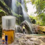 A person standing in front of a waterfall with an oil bottle.