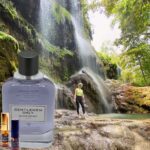 A man standing in front of a waterfall next to a bottle.