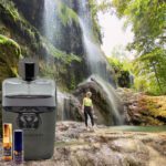 A man standing in front of a waterfall next to a bottle.