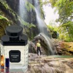 A man standing next to a waterfall with an ocean spray perfume bottle.