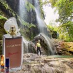 A woman standing in front of a waterfall next to a bottle.