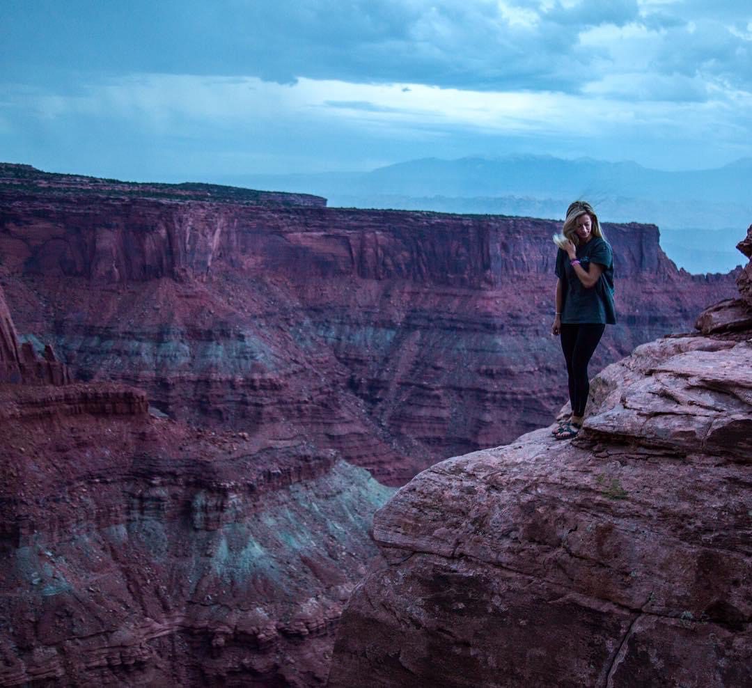 A woman standing on top of a cliff looking at the sky.