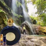 A person standing in front of a waterfall with a bottle of perfume.