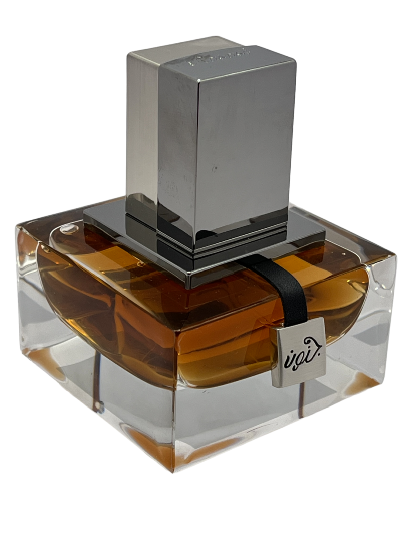 A square shaped bottle of perfume on top of a clear block.