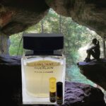 A bottle of perfume and a roll of parfum sitting in front of a cave.