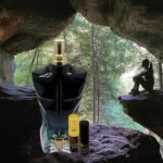 A black and gold bottle of perfume sitting in front of a cave.