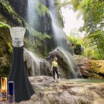 A person standing in front of a waterfall with a bottle and a dress.