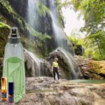 A person standing in front of a waterfall with a bottle.