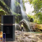 A man standing in front of a waterfall next to a bottle.