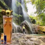 A person standing in front of a waterfall with a bottle and perfume.