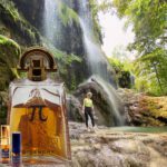 A bottle of perfume is in front of a waterfall.