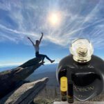 A person jumping in the air over rocks with a bottle of perfume.