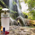 A person standing in front of a waterfall with a bottle of perfume.