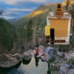 A person in the water next to rocks and a bottle of perfume.