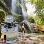 A person standing in front of a waterfall with a bottle.