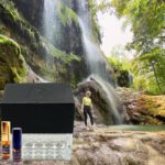 A person standing in front of a waterfall with bottles.