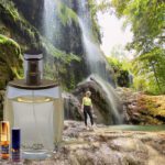 A person standing in front of a waterfall next to a bottle.