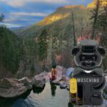 A bear is sitting in the water near some rocks.