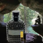 A bottle of perfume sitting in front of a cave.